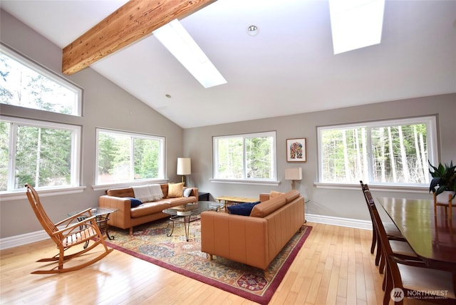 living area with lofted ceiling with skylight, light wood-style flooring, and baseboards