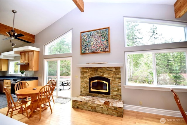 interior space with beam ceiling, high vaulted ceiling, light wood-style flooring, a stone fireplace, and baseboards