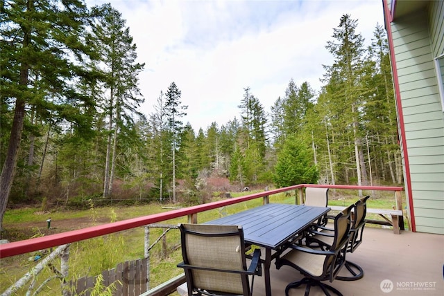 deck with outdoor dining space and a wooded view