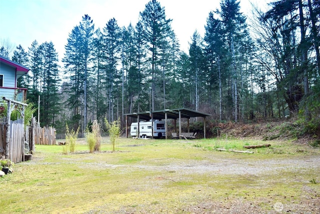 view of yard with a detached carport, fence, and a wooded view