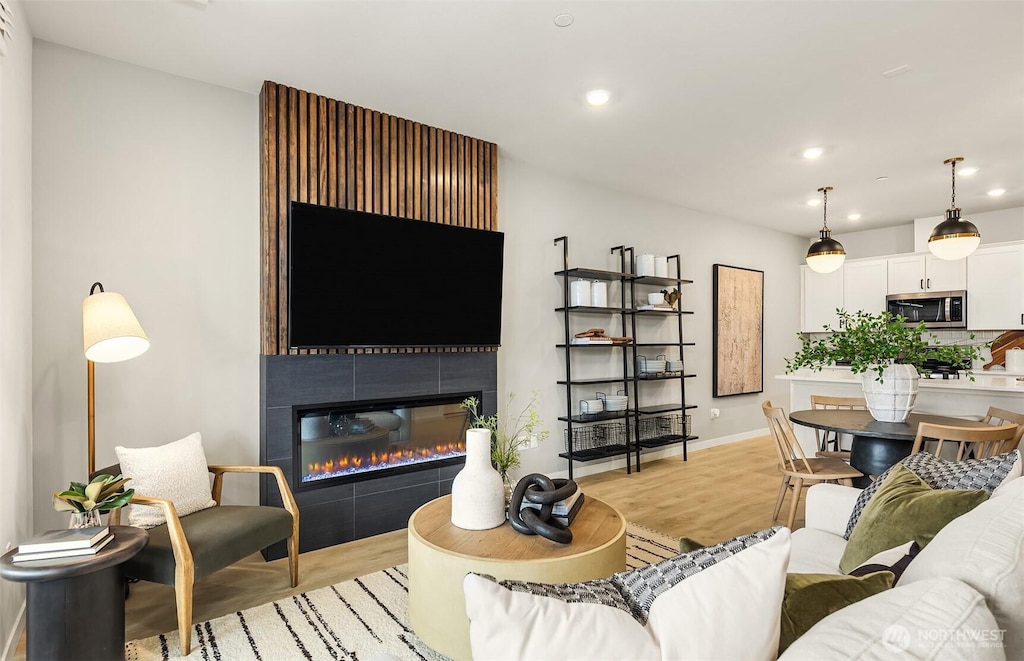 living area featuring a tiled fireplace, recessed lighting, baseboards, and light wood finished floors