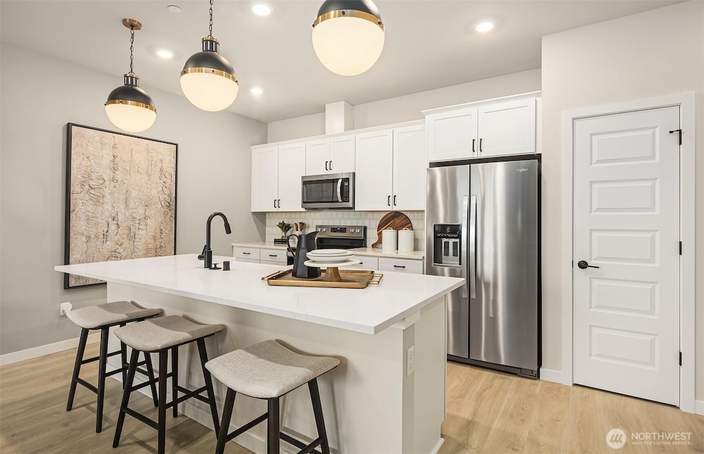 kitchen featuring light wood-style flooring, a center island with sink, backsplash, and stainless steel appliances