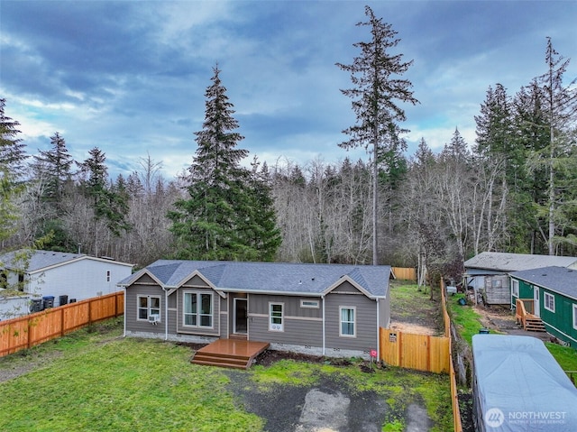 view of front of house with a view of trees, roof with shingles, a front lawn, and fence