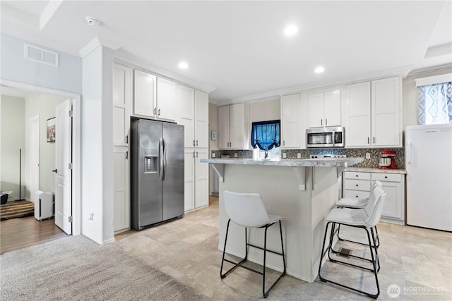 kitchen featuring visible vents, appliances with stainless steel finishes, white cabinetry, a kitchen breakfast bar, and a center island