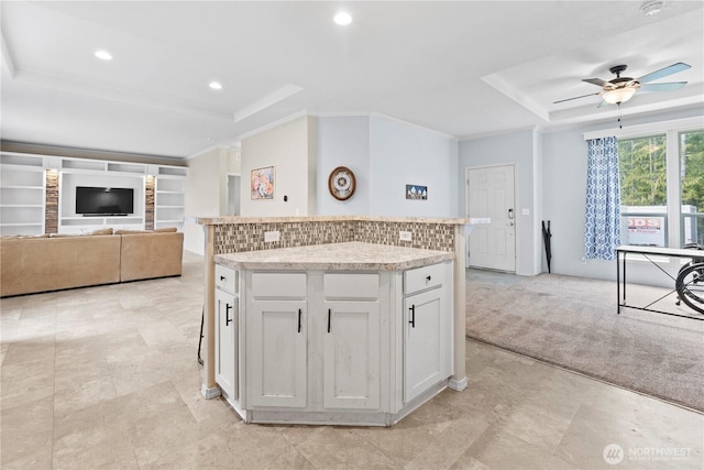 kitchen with ceiling fan, a raised ceiling, light colored carpet, and a kitchen island