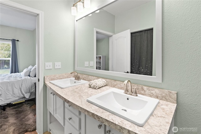 full bathroom featuring double vanity, connected bathroom, a textured wall, and a sink