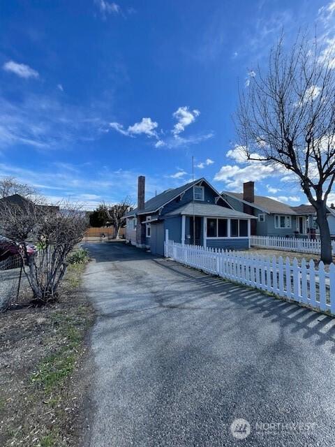 view of front of property featuring aphalt driveway, a fenced front yard, and a chimney