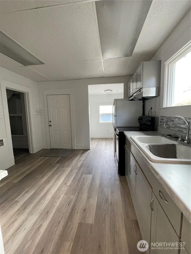 kitchen with baseboards, light wood finished floors, a sink, light countertops, and black electric range oven