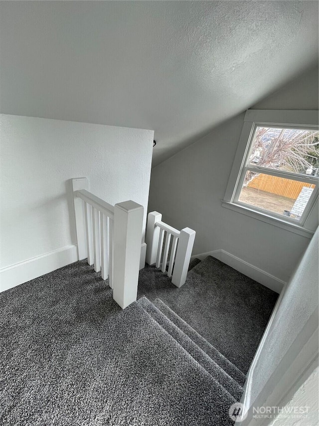 staircase with carpet flooring, a textured ceiling, baseboards, and vaulted ceiling