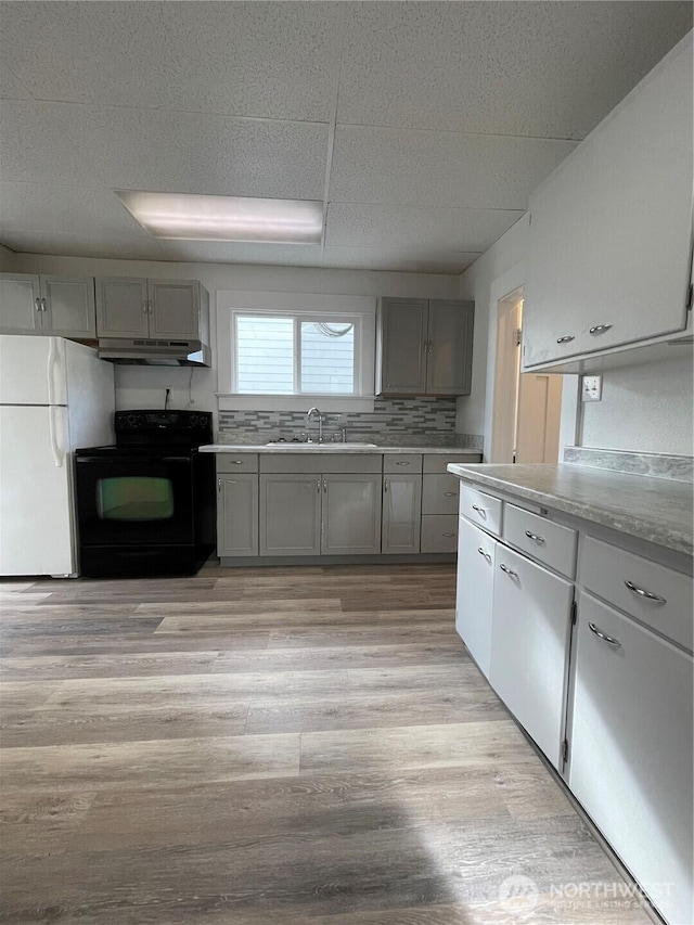 kitchen featuring gray cabinetry, under cabinet range hood, a sink, black range with electric cooktop, and freestanding refrigerator