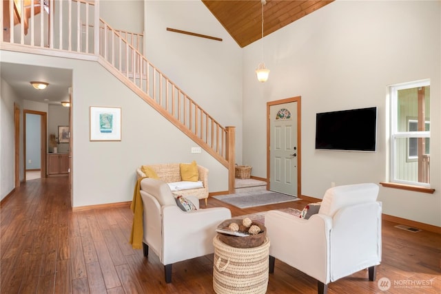 living area featuring visible vents, high vaulted ceiling, hardwood / wood-style flooring, baseboards, and stairs