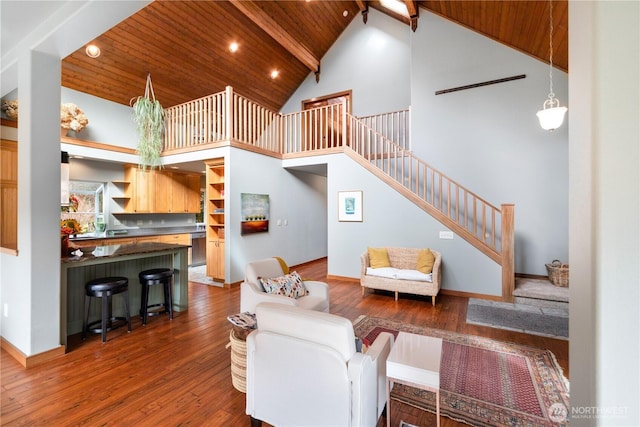 living area with beam ceiling, high vaulted ceiling, hardwood / wood-style flooring, stairway, and wooden ceiling