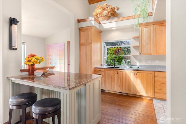 kitchen with open shelves, light brown cabinetry, a sink, light wood-style floors, and a kitchen bar