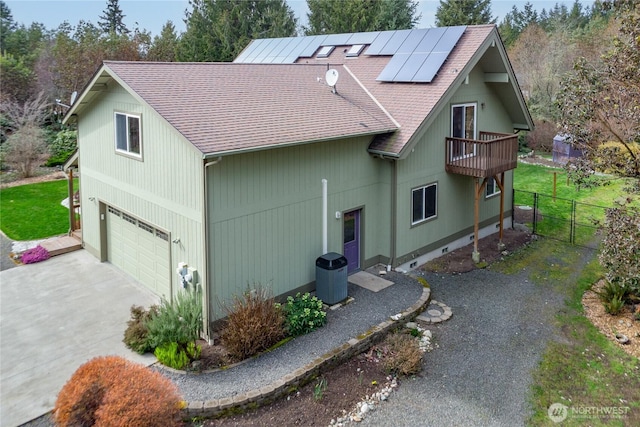 view of side of home with solar panels, concrete driveway, a garage, and roof with shingles