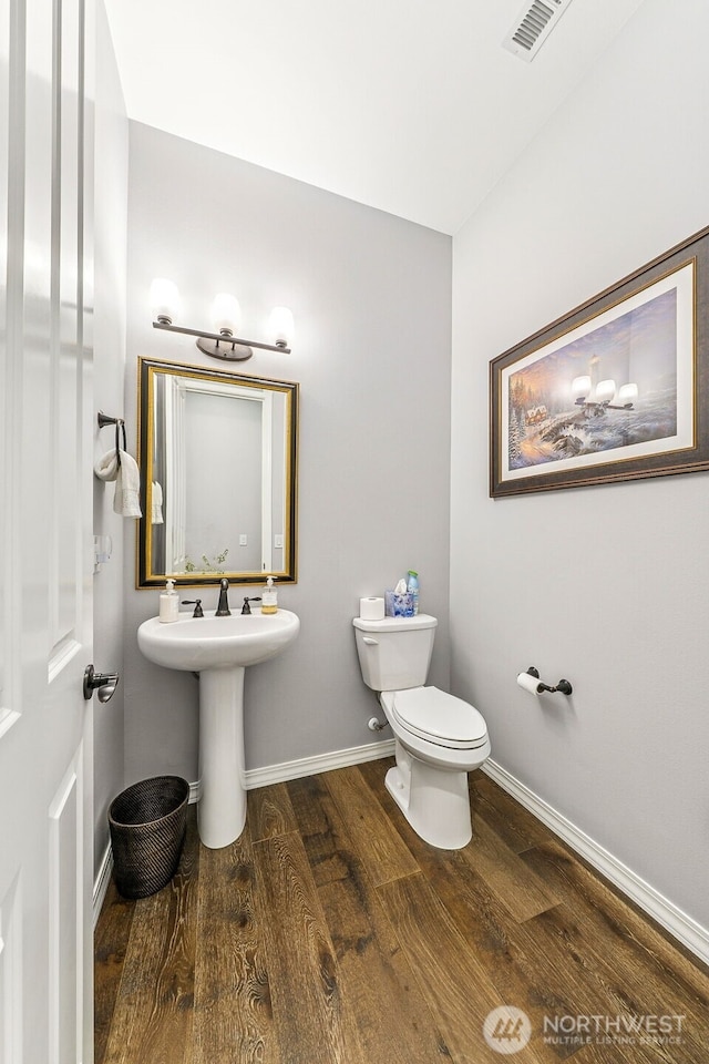 half bathroom with baseboards, visible vents, wood finished floors, and toilet