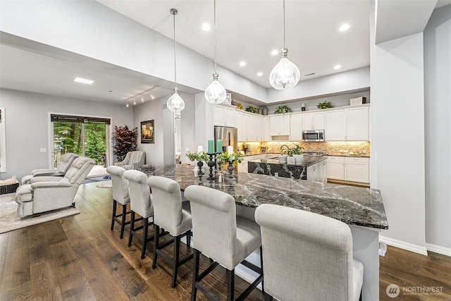 kitchen featuring a spacious island, stainless steel appliances, white cabinets, dark wood-style flooring, and open floor plan