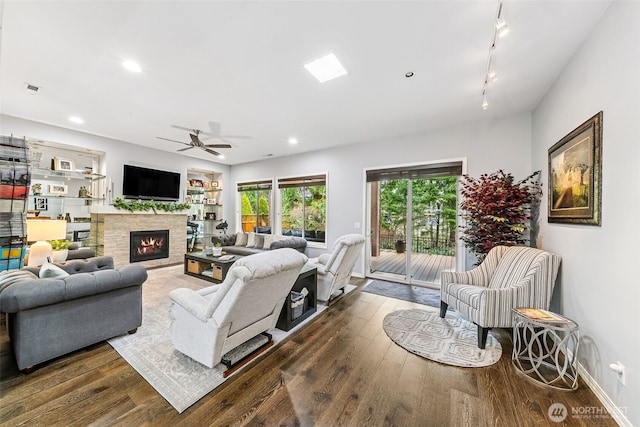 living area featuring wood finished floors, ceiling fan, rail lighting, and a warm lit fireplace