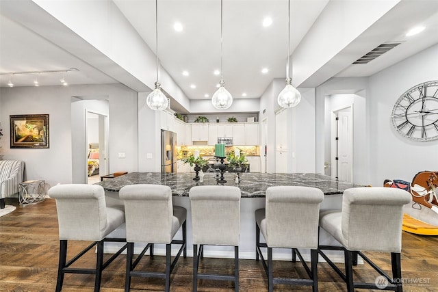 kitchen with white cabinetry, a breakfast bar, visible vents, dark wood finished floors, and stainless steel fridge