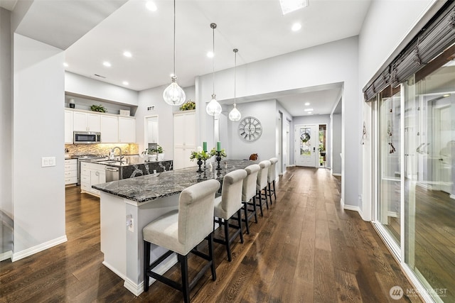 kitchen with a sink, stainless steel appliances, dark wood-style floors, a kitchen bar, and a large island