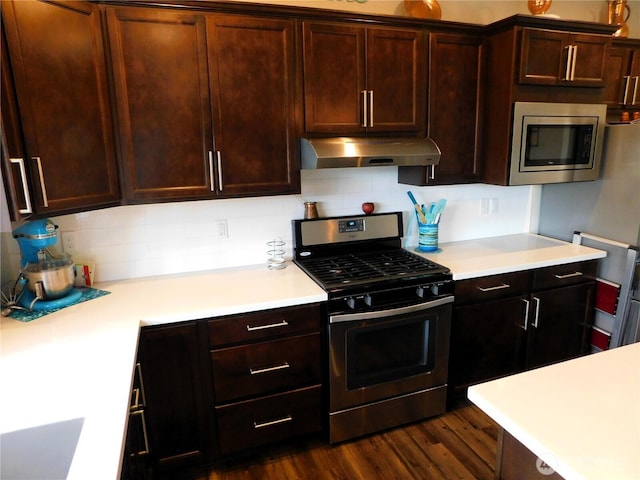 kitchen featuring dark wood finished floors, stainless steel appliances, light countertops, under cabinet range hood, and backsplash