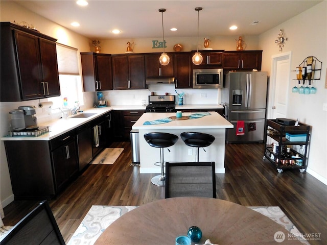 kitchen with a sink, under cabinet range hood, light countertops, appliances with stainless steel finishes, and dark wood-style flooring