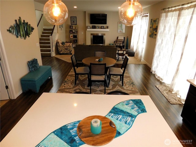 dining room featuring stairway, baseboards, dark wood-style floors, and a fireplace