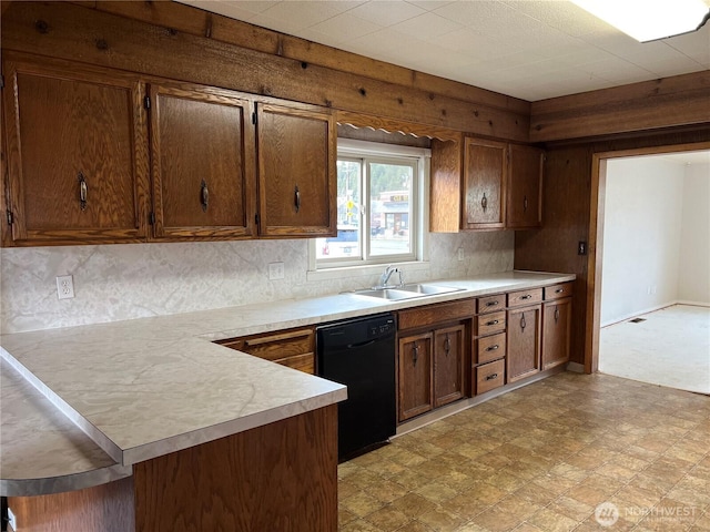 kitchen with light countertops, a peninsula, black dishwasher, light floors, and a sink
