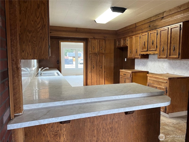 kitchen featuring a peninsula, light countertops, a sink, and brown cabinets