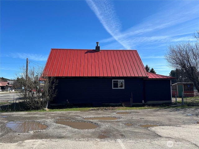 view of property exterior with an outdoor structure, fence, metal roof, a barn, and a garage