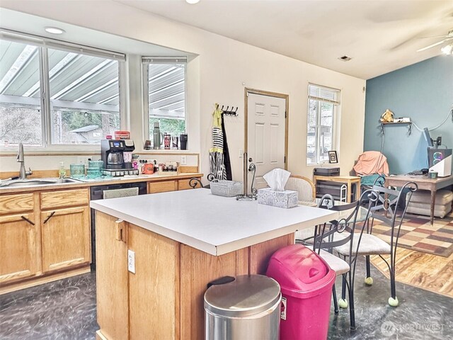 kitchen with a breakfast bar area, a kitchen island, dark wood-style flooring, a sink, and light countertops