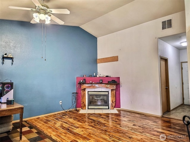 living area with a ceiling fan, wood finished floors, visible vents, a fireplace with flush hearth, and vaulted ceiling