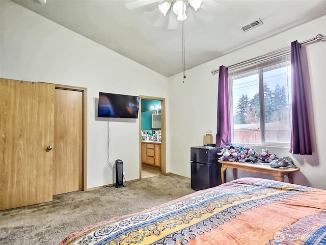 bedroom with a ceiling fan, visible vents, freestanding refrigerator, vaulted ceiling, and light carpet