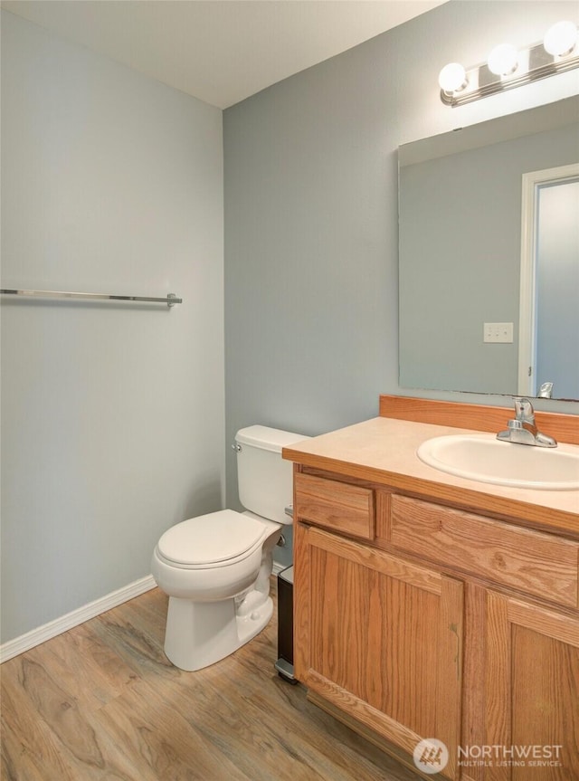 half bathroom with toilet, vanity, baseboards, and wood finished floors