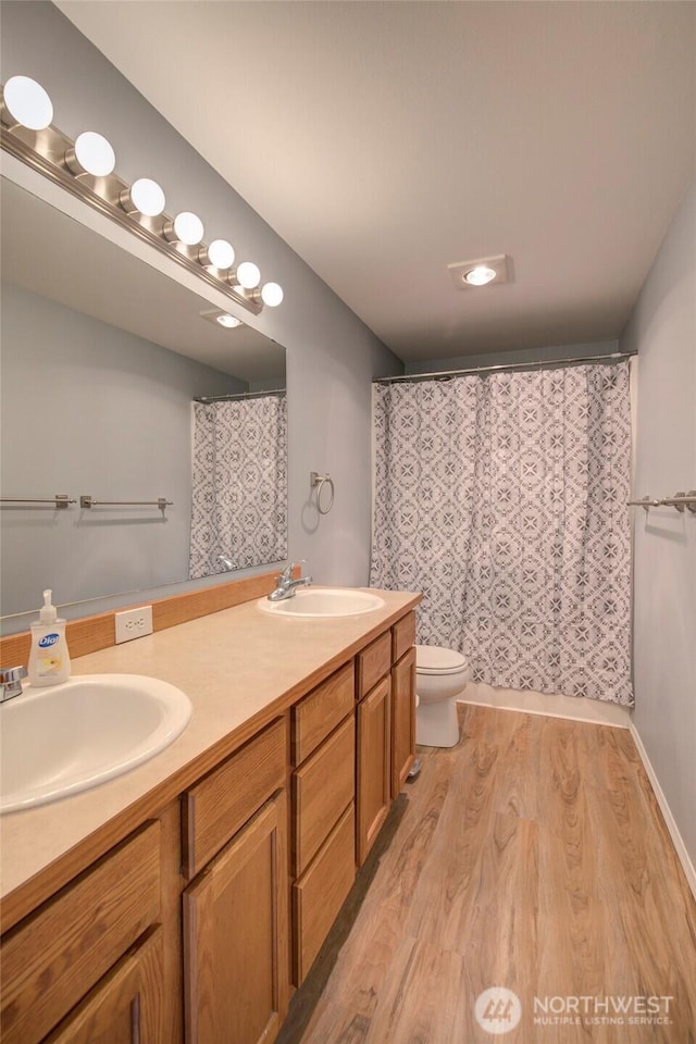 full bath with a sink, toilet, wood finished floors, and double vanity