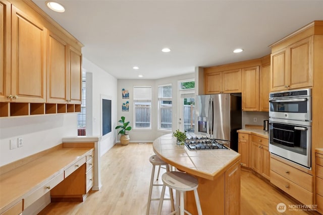 kitchen featuring tile countertops, appliances with stainless steel finishes, light wood-type flooring, and light brown cabinets