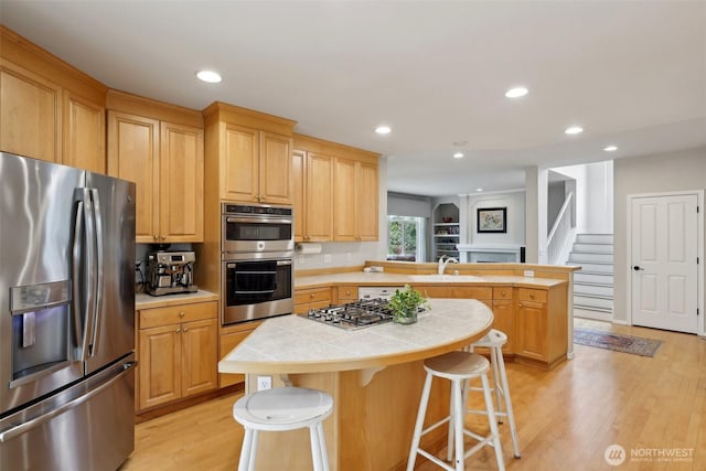 kitchen with light wood-type flooring, a peninsula, tile counters, stainless steel appliances, and recessed lighting