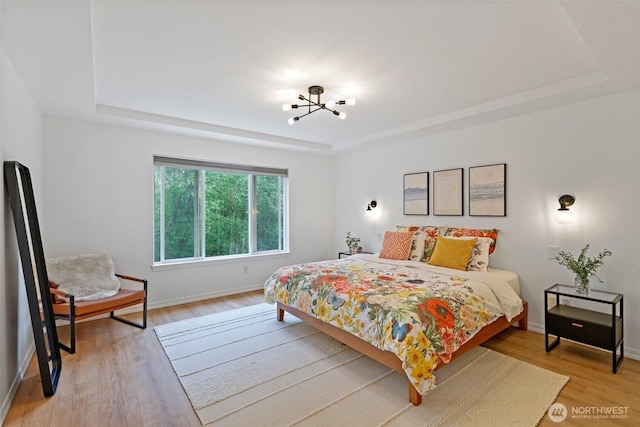 bedroom featuring a tray ceiling, a chandelier, and light wood finished floors