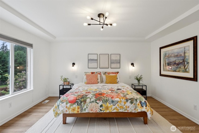 bedroom with baseboards, a notable chandelier, a tray ceiling, and light wood-type flooring