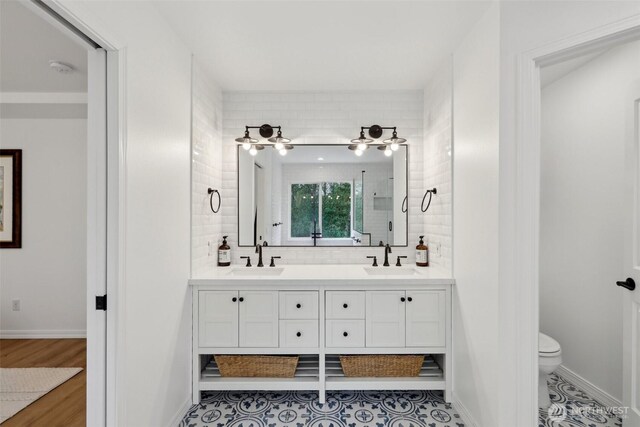 bathroom featuring baseboards, double vanity, toilet, and a sink