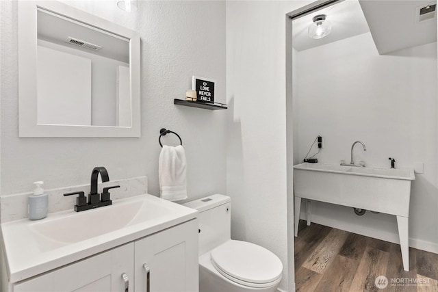 bathroom with vanity, toilet, wood finished floors, and visible vents