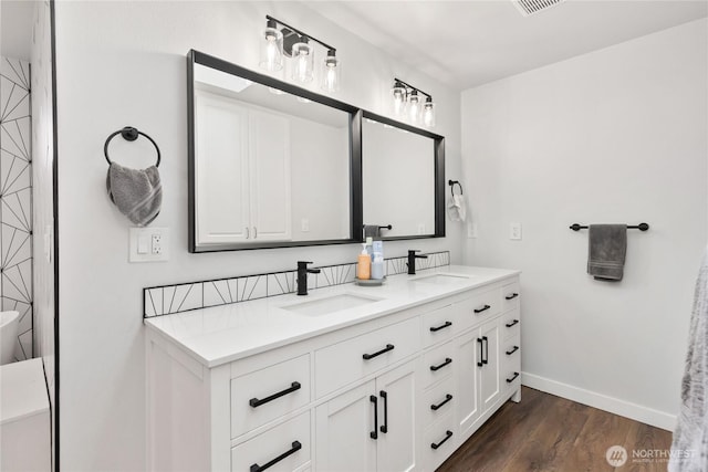 bathroom featuring double vanity, wood finished floors, baseboards, and a sink