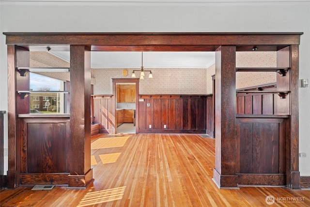interior space featuring visible vents, light wood-style floors, ornamental molding, and wallpapered walls