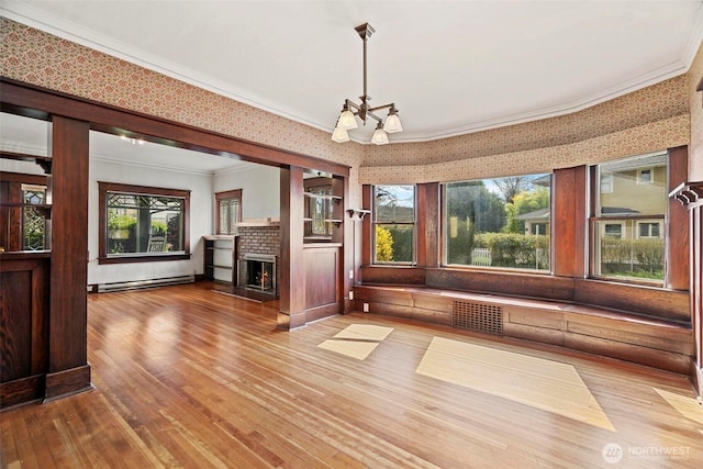 unfurnished dining area with hardwood / wood-style flooring, a baseboard heating unit, crown molding, a brick fireplace, and a chandelier