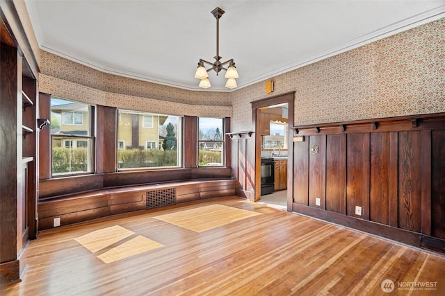 empty room featuring a chandelier, light wood finished floors, wallpapered walls, and ornamental molding