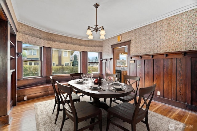 dining space featuring light wood finished floors, a chandelier, crown molding, and wallpapered walls