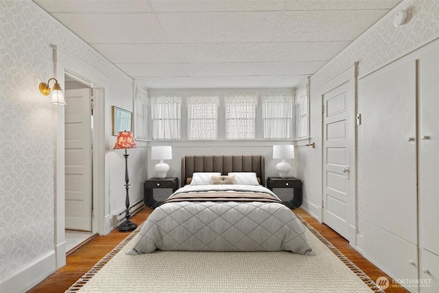 bedroom featuring multiple windows, wallpapered walls, a paneled ceiling, and wood finished floors