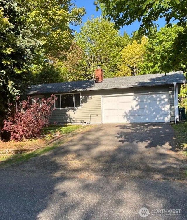 ranch-style house featuring a chimney, driveway, and an attached garage