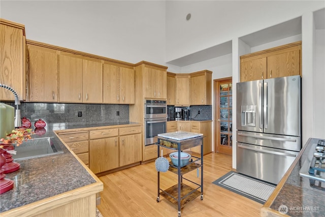 kitchen featuring decorative backsplash, dark countertops, light wood-style floors, and appliances with stainless steel finishes