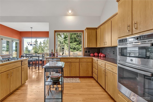 kitchen with light wood finished floors, decorative backsplash, stainless steel appliances, and a notable chandelier