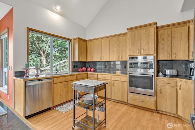 kitchen featuring tasteful backsplash, light wood-type flooring, appliances with stainless steel finishes, high vaulted ceiling, and a sink